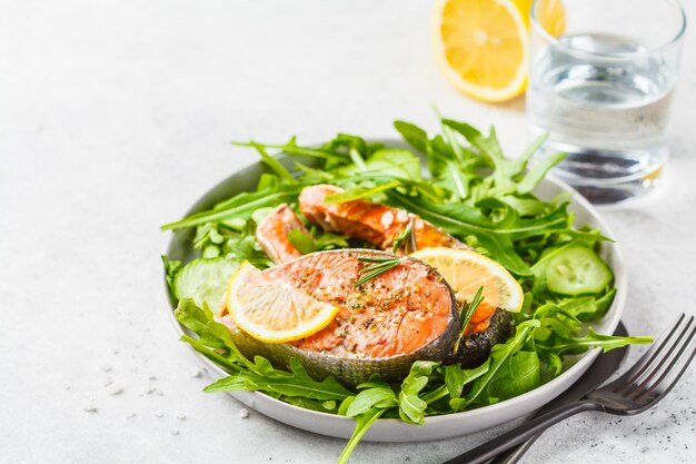 Poisson rouge frit avec salade de roquette et concombre dans une assiette blanche, espace de copie.