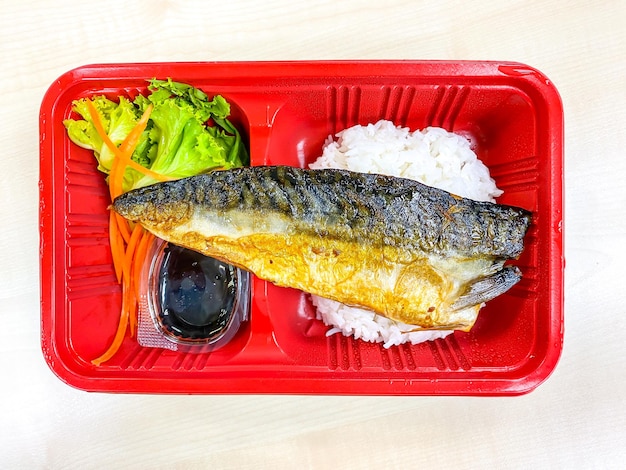 Poisson Saba grillé avec salade dans le récipient alimentaire sur la table