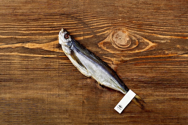 Poisson sabre séché salé avec étiquette en papier sur la queue allongée sur une surface en bois