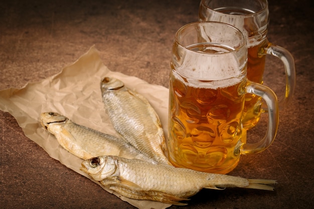 Poisson séché en gros plan, verre de bière vintage sur fond de papier et marron. Format horizontal