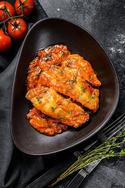 Poisson Tilapia cuit au four dans les tomates sur une assiette. Fond noir. Vue de dessus.