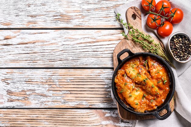 Poisson Tilapia cuit dans des tomates dans une casserole. Fond en bois blanc. Vue de dessus. Copiez l'espace.