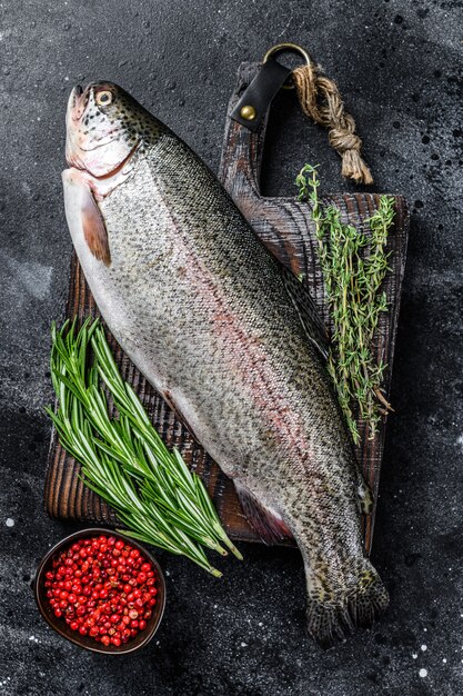 Poisson truite arc-en-ciel cru sur une planche à découper avec des herbes. Vue de dessus.