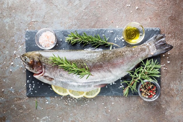 Poisson truite cru sur ardoise avec romarin et citron sur une table en pierre, vue de dessus