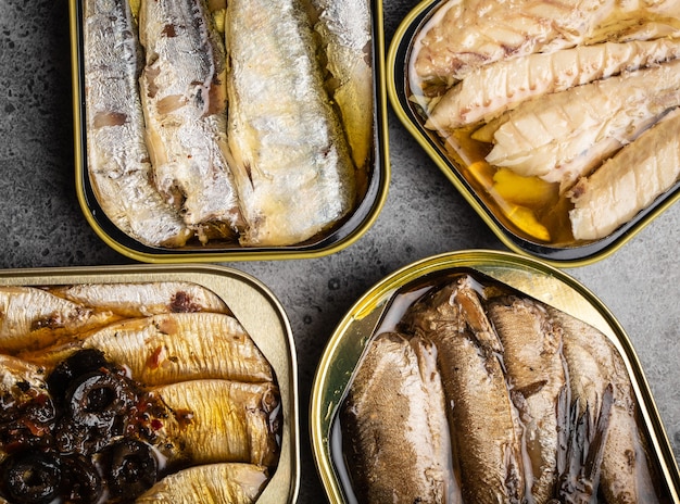 Poissons en conserve assortis dans une boîte sur fond de béton gris : sardine, sardine fumée, maquereau. Le poisson en conserve est un aliment pratique, rapide et sain et une source d'acides gras oméga-3, de protéines et de vitamine D