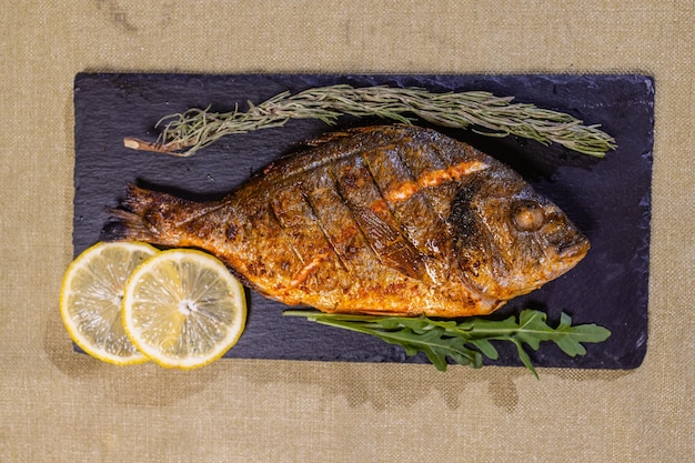 Poissons dorés rôtis au citron, herbes, sel sur fond noir. Concept d'alimentation saine. Cadre alimentaire.