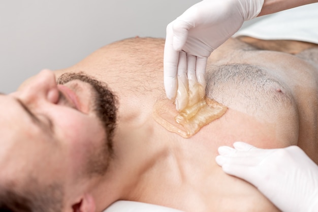 Poitrine D'épilation De Jeune Homme Avec De La Pâte De Cire Liquide Par Les Mains D'une Cosmétologue Dans Un Salon De Beauté