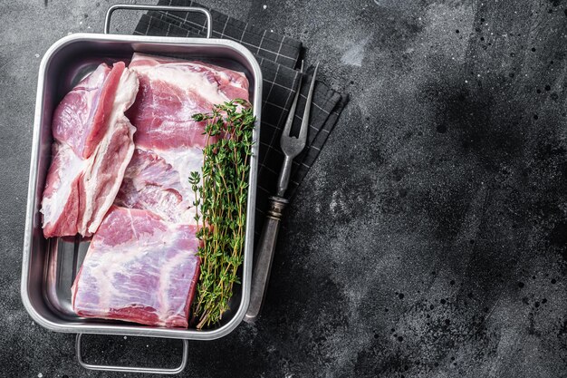 Poitrine de porc crue fraîche avec peau dans un plateau en acier avec des herbes Fond noir Vue de dessus Espace de copie