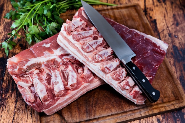 Poitrine de porc frais sur une planche à découper utilisée reposant sur une vieille table en bois