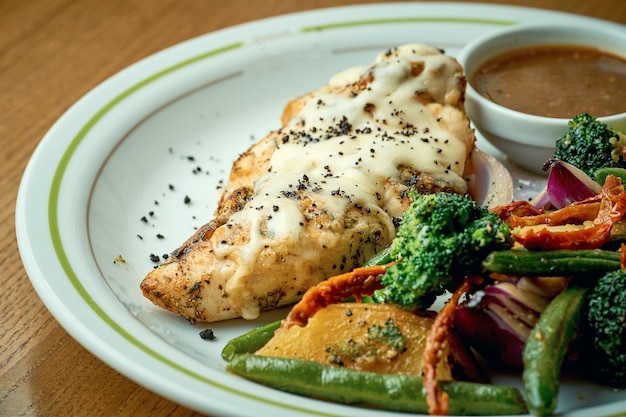 Poitrine de poulet au four avec fromage et légumes bouillis, brocoli dans une assiette blanche sur une table en bois