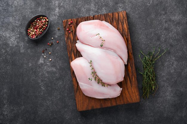 Photo poitrine de poulet filets de poitrine de poulet crus sur une planche à découper en bois avec des herbes et des épices sur fond noir vue de dessus avec espace de copie