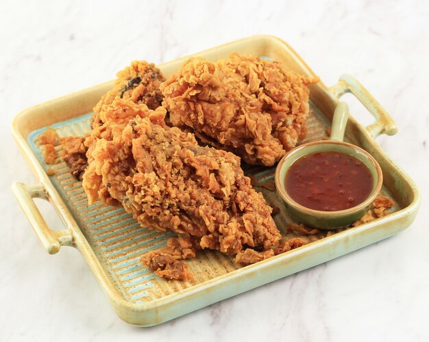 Poitrine de poulet frite croustillante dorée et ailes de poulet, servies sur une assiette carrée rustique avec sauce chili, isolée sur fond blanc avec espace de copie pour le texte