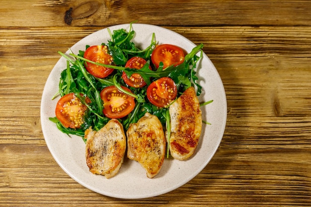 Poitrine de poulet frite avec salade de roquette fraîche et tomates cerises sur table en bois Vue de dessus