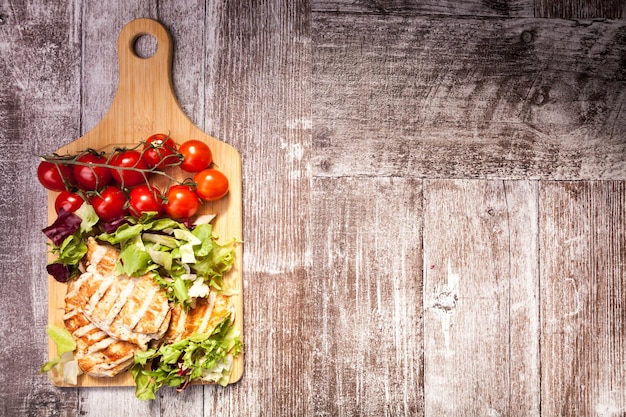 Poitrine de poulet grillée sur salade fraîchement coupée à côté d'un bouquet de tomates sur une planche de bois