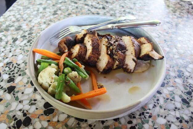 Photo poitrine de poulet grillée avec des tranches de carottes, du brocoli et des haricots longs sur une assiette blanche prête à manger.