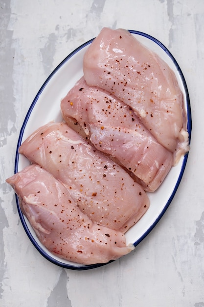 Photo poitrines de poulet crues sur un plat blanc sur une surface en céramique