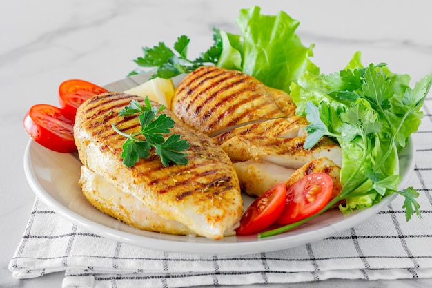 Poitrines de poulet grillées servies sur une assiette avec salade et légumes.