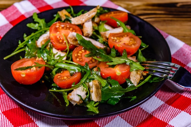 Poitrines de poulet rôties et salade de roquette et tomates cerises dans une assiette noire