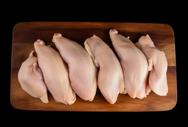 Poitrines de poulet à la viande fraîche allongées sur une planche de cuisine et un fond noir