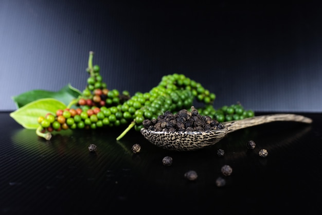 Poivre frais et poivre noir à la cuillère en bois sur fond noir.