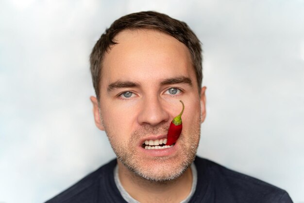 Poivre rouge chaud dans la bouche portrait en gros plan d'un jeune homme mangeant du piment