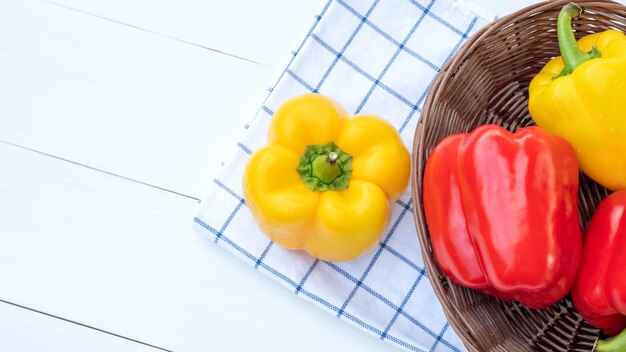 Poivron jaune et rouge sur une table en bois blanche.