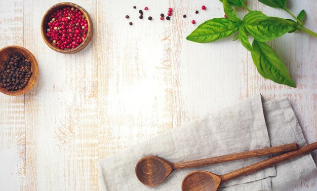 Poivron noir et rouge, feuilles de basilic, carottes, poêle en céramique, support en bois, vieilles cuillères simples et serviette en lin sur fond clair. Concept d'accessoires de cuisine. Mise au point sélective. Vue de dessus. Image tonique