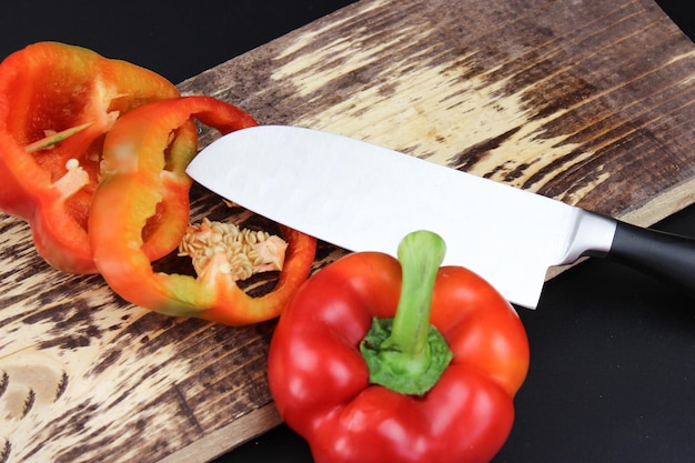 Poivron rouge et couteau de cuisine sur une planche à découper en bois Cuisiner un repas sain Le couteau coupe un poivron en deux