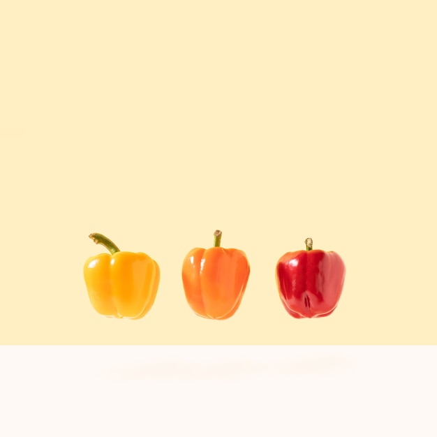 Poivron rouge orange et jaune en lévitation sur fond pastel lumineux Concept alimentaire minimal