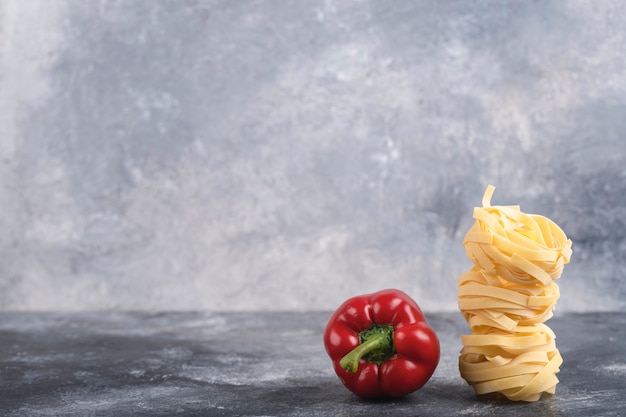 Poivron rouge avec pâtes tagliatelles crues sur marbre.