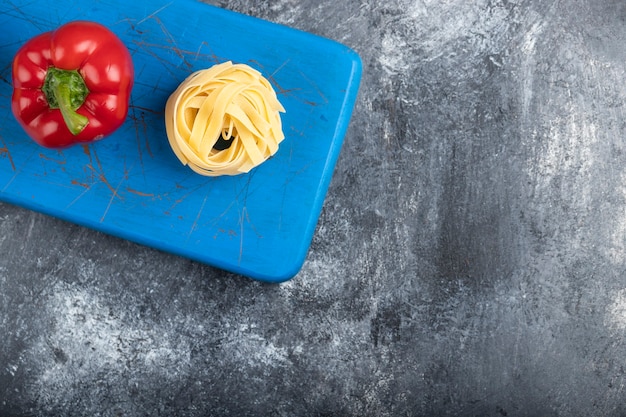 Poivron rouge avec des pâtes tagliatelles crues sur une planche à découper bleue.