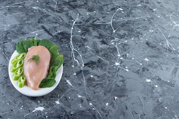 Poivron tranché, épinards et poitrine de poulet sur une assiette, sur fond de marbre.