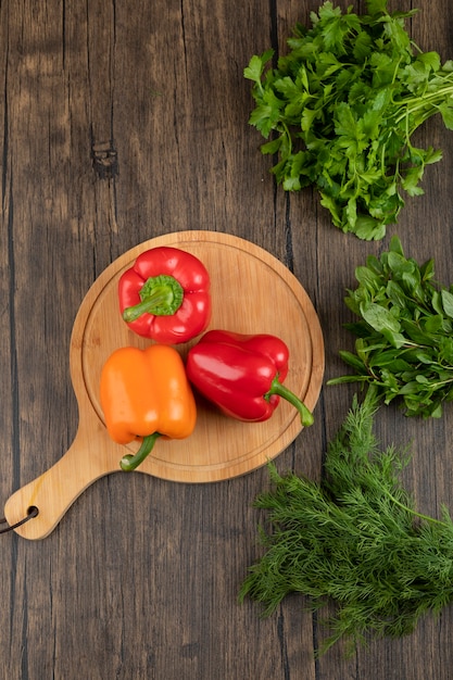 Poivrons colorés sur planche de bois avec des verts frais