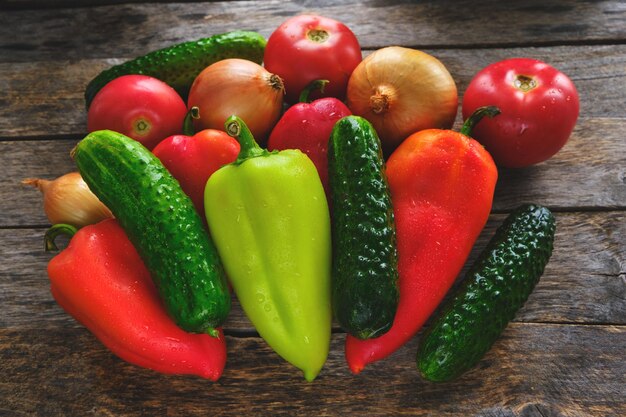 Poivrons, concombres, oignons et tomates sur un vieux fond en bois.