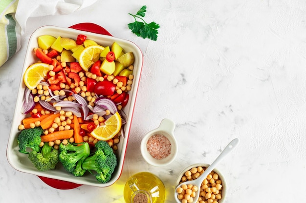 Poivrons crus pommes de terre brocoli pois chiches et oignons avec de l'huile et des épices dans un plat à cuire