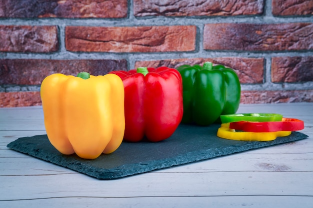 Poivrons de différentes couleurs jaune rouge et vert sur table en pierre noire au-dessus d'une table en bois et mur de briques