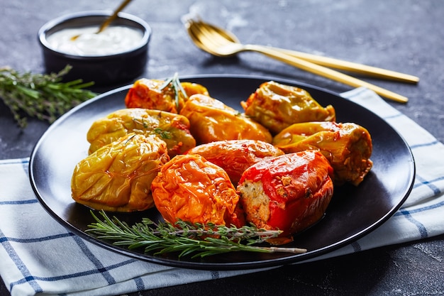 Poivrons farcis classiques avec riz, boeuf haché et porc à la sauce tomate, romarin et thym sur une plaque noire avec de la crème sure