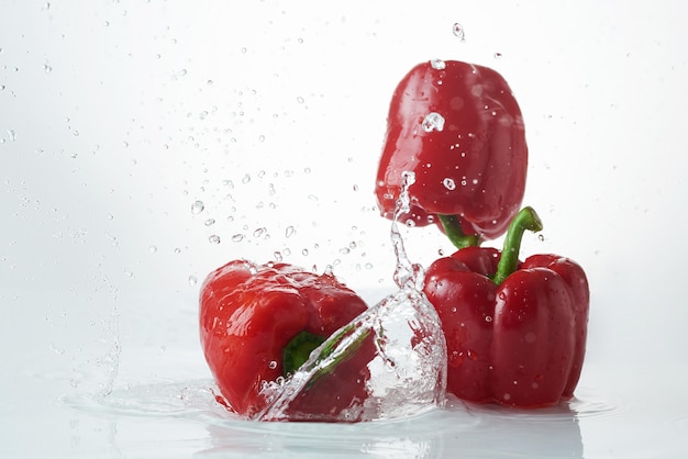 Poivrons frais tombant dans l'eau claire. Poivron rouge frais dans une éclaboussure d'eau sur fond blanc.