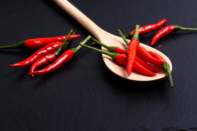 Poivrons piments rouges thaïlandais en cuillère de bois sur fond de pierre ardoise noire