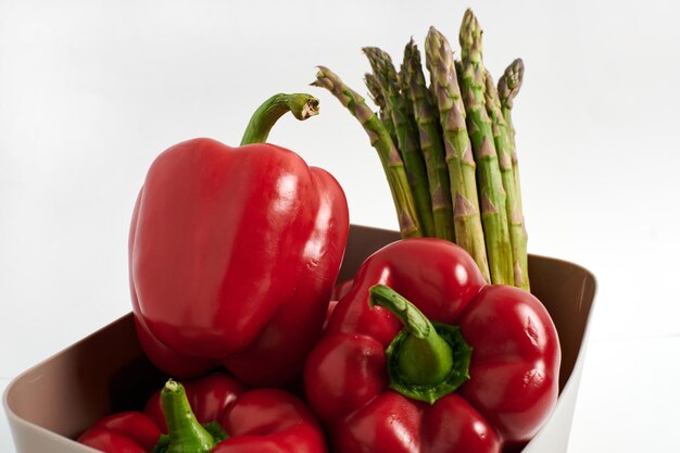 Poivrons rouges et asperges dans un récipient en plastique sur fond blanc