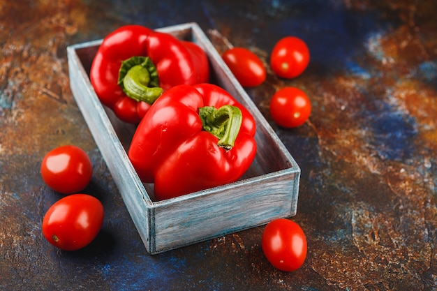 Poivrons rouges dans une boîte en bois et tomates sur fond noir