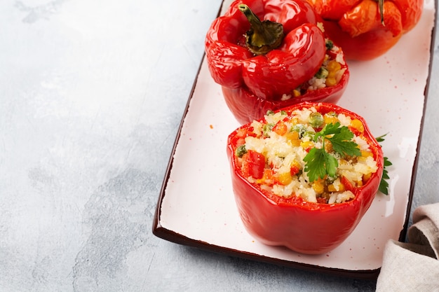 Poivrons rouges farcis de riz et de légumes sur un bol en céramique sur béton gris