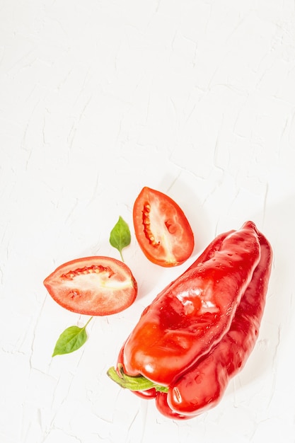 Photo poivrons rouges géants et tomates sur fond blanc. légume sucré, nouvelle récolte, ingrédient frais pour une alimentation saine, vue de dessus