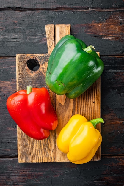 Poivrons verts, rouges et jaunes colorés, sur le vieux fond de table en bois foncé, vue de dessus à plat