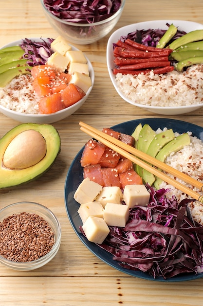 Poke bol nourriture hawaïenne. une assiette de riz, saumon, avocat, chou et fromage. à côté du sésame et de l'avocat frais sur une table en bois naturel