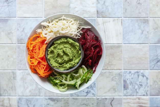 Poke bol végétarien fait maison carottes crues fraîches, chou, concombre et betteraves avec pesto, régime alimentaire, aliments sains sur fond de carreaux de céramique. Vue de dessus, gros plan