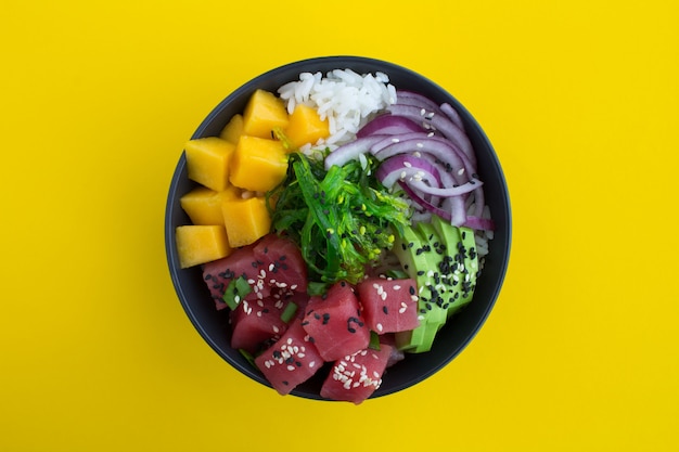 Poke bowl avec du thon dans le bol sombre au centre de l'arrière-plan jaune.Vue de dessus.Gros plan.