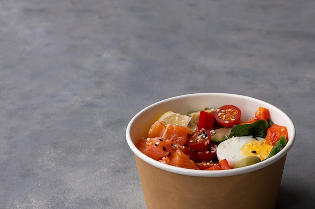 Poke bowl à emporter avec saumon frais, avocat, quinoa et légumes dans un emballage en papier kraft recyclé
