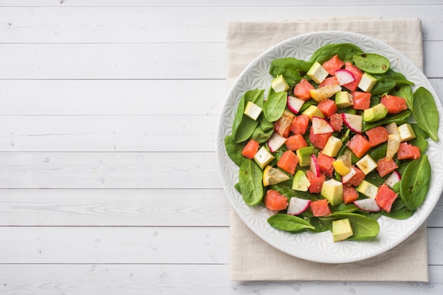 Poke Salade hawaïenne avec du saumon, des épinards à l&#39;avocat et des légumes dans une assiette sur une table blanche.