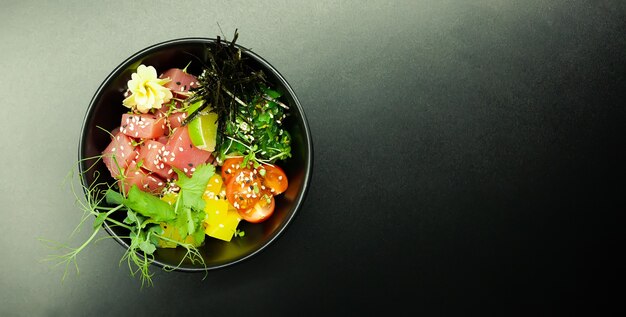 Poke salade de thon dans un bol. Ingrédients Thon frais, tomates cerises, algues marinées, riz, takuan, sauce Ponzu, sauce Teriyaki, nori, graines de sésame, citron vert, coriandre. Concept de salade de fruits de mer asiatique.